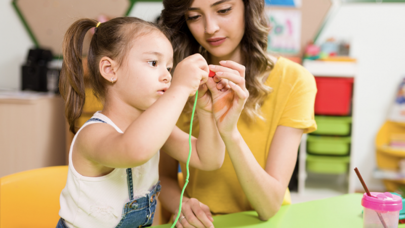 Child stringing beads with adult helping